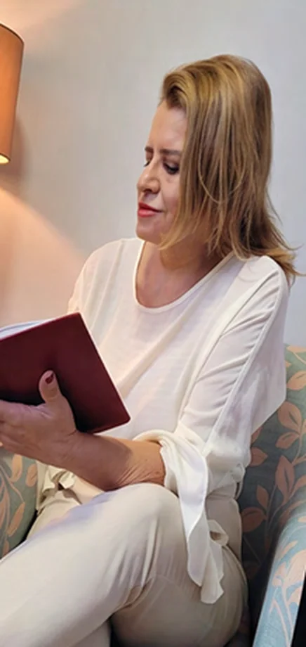 Sylvana Melo lendo, sentada numa poltrona do consultório